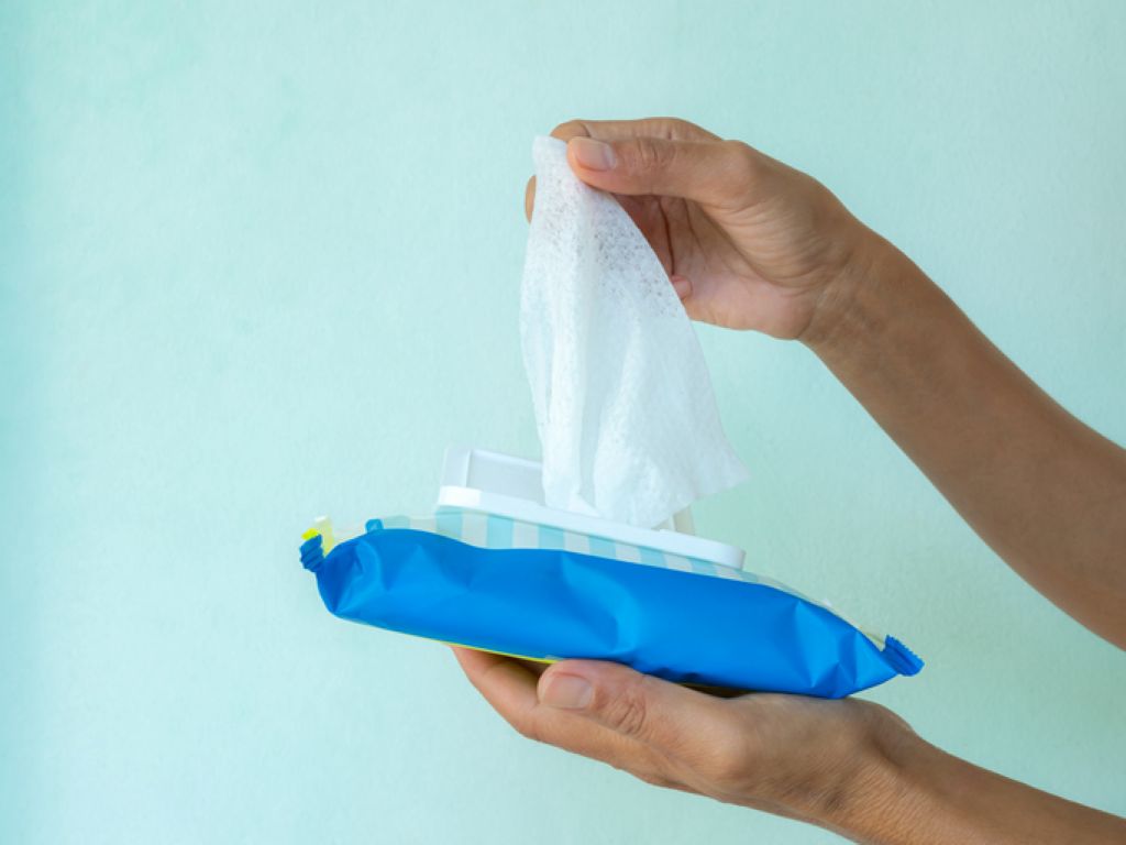 A person pulls a wet wipe from a blue plastic package against a light blue background.